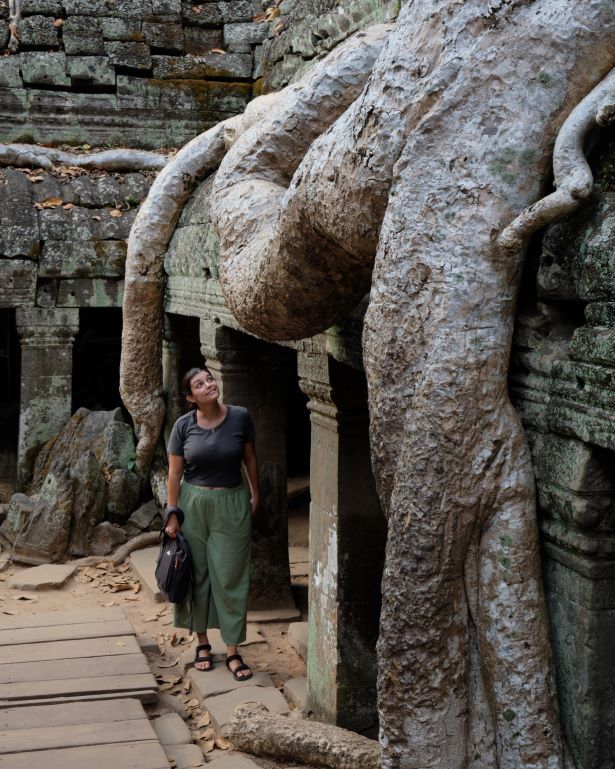 Mujer mira una raíz de un árbol que crece encima de una edificación del templo de Ta Prohm, en Angkor, Camboya