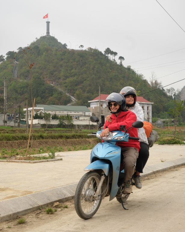 Dos personas en moto con la bandera de Vietnam al fondo, en Lung Cu, el punto mas septentrional de Vietnam. Loop de Ha giang