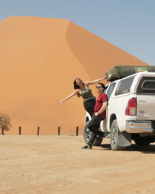 Dos personas posan junto a su coche 4x4 con tienda de techo con la duna 45 de fondo, cerca de Sossusvlei, Namibia