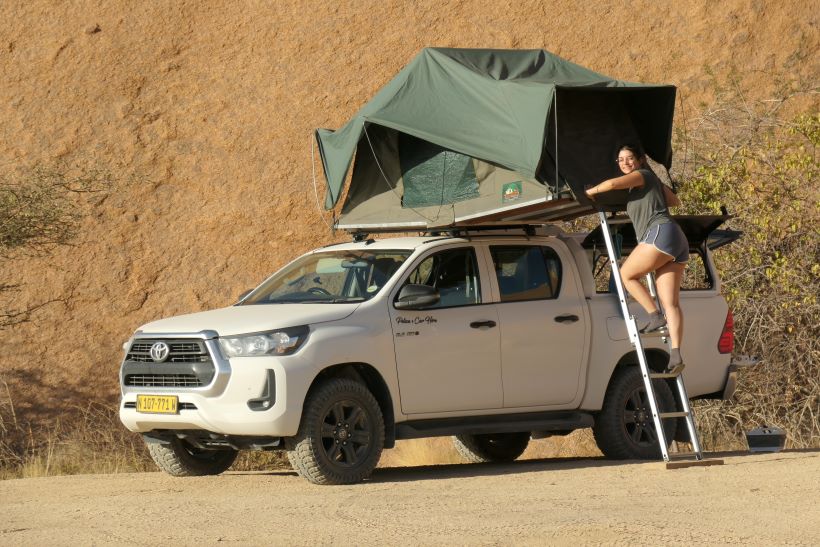 Mujer asciende a tienda de techo en toyota hilux 4x4 en namibia